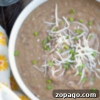 A bowl of creamy pressure cooker refried beans topped with shredded cheese and chopped chives sits next to a floral napkin.