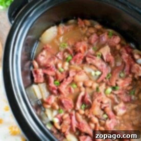 A slow cooker brimming with ham and beans, featuring tender pinto beans, diced ham, and green onions nestled in a savory broth.