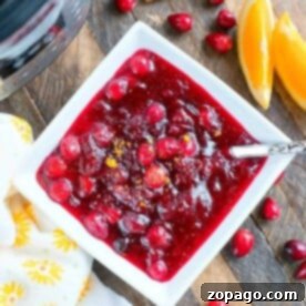 A square bowl of Instant Pot cranberry sauce adorned with orange slices, cinnamon sticks, and fresh cranberries.