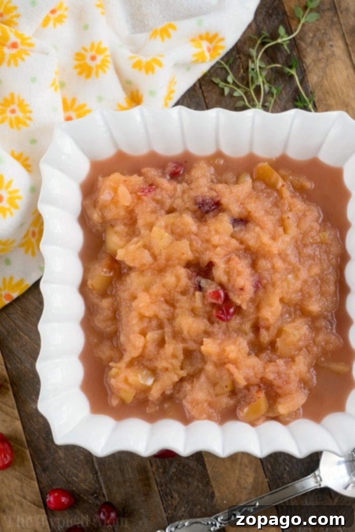 This Instant Pot cranberry applesauce is a great Thanksgiving or Christmas side dish or snack throughout the year. It's a great sweet homemade treat. #instantpot #instantpotrecipes #thetypicalmom #cranberry #applesauce #homemade #pressurecooker #crockpotexpress A serving of homemade cranberry applesauce in a small glass dish, garnished with fresh cranberries.