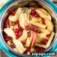 Sliced apples and cranberries simmering in an instant pot on a rustic wooden surface.