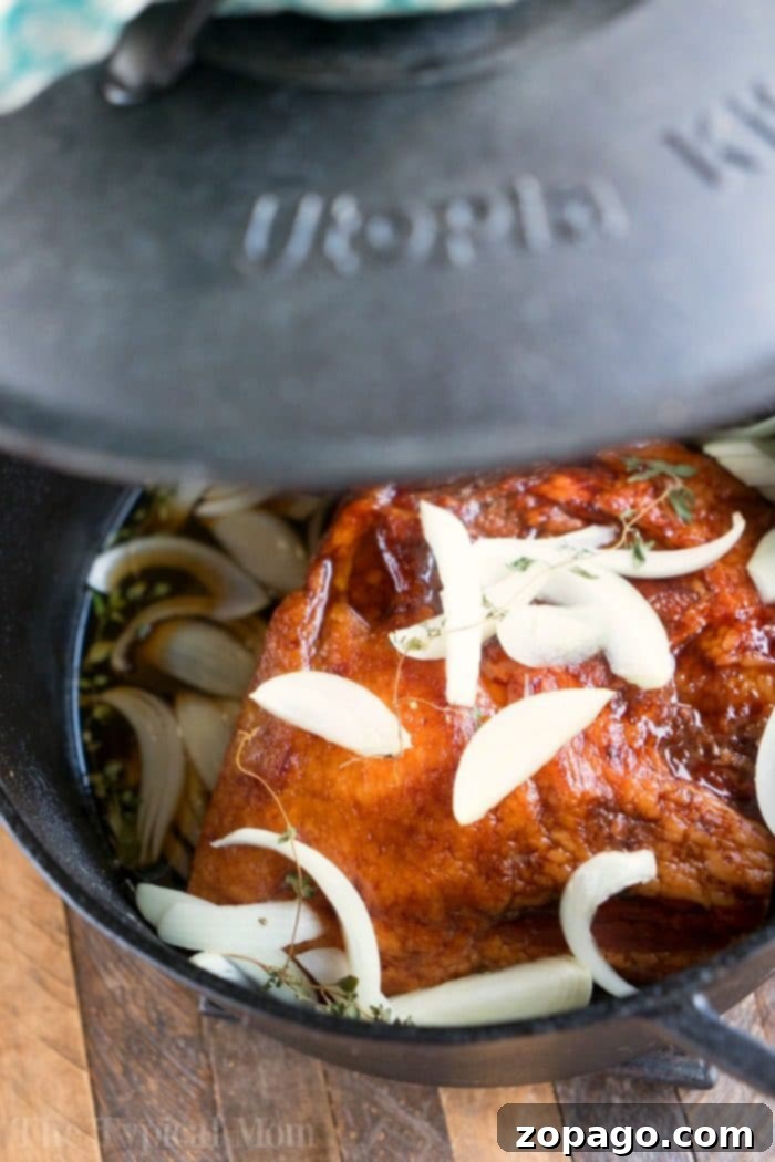 This Dutch oven ham needs to go on your list of the best Dutch oven recipes this year, and with a honey glaze it is perfect for Christmas or Easter dinner. #dutchoven #ham #dutchovenrecipes #honeyham A ham in a Dutch oven with sliced onions and herbs.