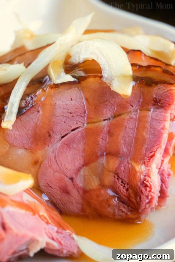The exquisite honey glaze and savory onions elevate this Dutch oven ham. Close-up of a perfectly glazed ham topped with sliced onions and herbs, reminiscent of a hearty Dutch oven ham, ready to be served.