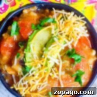 Easy Instant Pot Turkey Soup 3 A bowl of Instant Pot turkey soup topped with sliced avocado, shredded cheese, and chopped cilantro. The bowl rests on a wooden surface next to a colorful, patterned fabric. The soup features chunks of vegetables in a rich tomato-based broth.