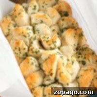 Tear-and-Share Bread 2 Golden, bite-sized Refrigerated Biscuit Pull Apart Bread pieces topped with parsley in a parchment-lined baking dish.