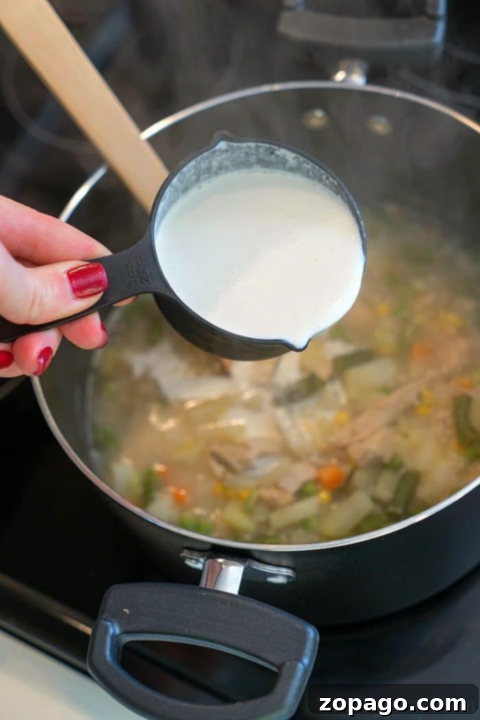 A bowl of creamy turkey pot pie soup, topped with a halved golden-brown biscuit, ready to be enjoyed.