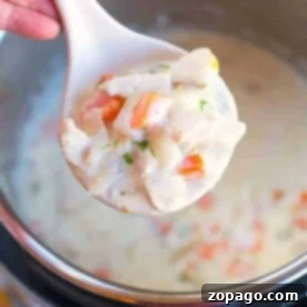 A ladle of creamy turkey pot pie soup brimming with vegetables hovers over a steaming pot.