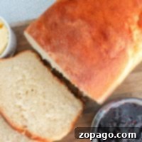 Freshly baked bread loaf with slices, alongside butter and a jar of berry jam on a wooden board, captures the cozy essence of baking bread at home.