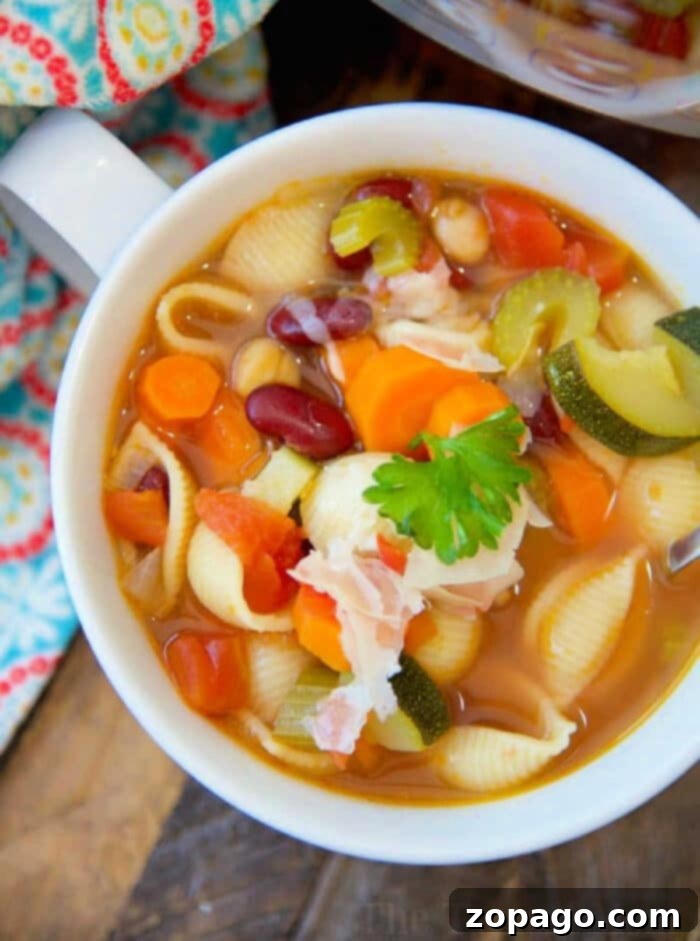 Quick Pressure Cooker Vegetable Soup 2 A vibrant bowl of pressure cooker vegetable soup, featuring shell pasta, kidney beans, zucchini, carrots, celery, and diced tomatoes, garnished with fresh parsley and a slice of crispy bacon, set against a warm, rustic backdrop.