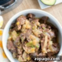French Onion Fondant Roast 4 A bowl of shredded beef with onions, reminiscent of French onion flavors, is served beside an avocado half on a wooden surface.