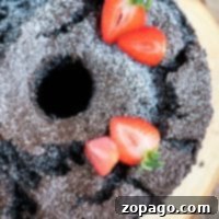 Chocolate angel food bundt cake dusted with powdered sugar, topped with sliced strawberries on a wooden board.