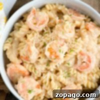 A bowl of creamy instant pot shrimp Alfredo with spiral-shaped noodles, garnished with grated cheese and small bits of herbs.