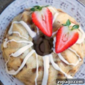 A bread pudding bundt cake with white icing, topped with halved strawberries, sits gracefully on a decorative plate, reminiscent of the cozy warmth that instant pot bread pudding brings to a home.