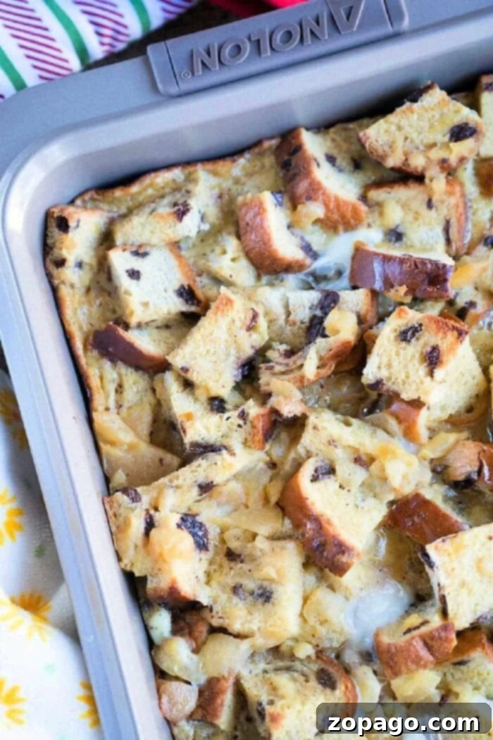 Homestyle Raisin Bread Pudding 2 A baking pan filled with a delightful raisin bread pudding, featuring cubed bread pieces, some toasted. The mix of bread and creamy custard is studded with raisins and perhaps chocolate chips. The pan rests on a vibrant, colorful tablecloth.