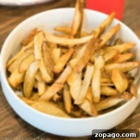 A bowl of golden-brown homemade French fries, perfectly crisped using the Ninja Foodi, sits invitingly on a wooden table.