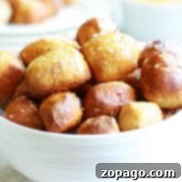 A white bowl filled with air fryer pretzel bites, perfectly salted, with a cheese dipping sauce in the background.