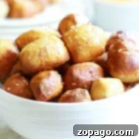 A white bowl filled with air fryer pretzel bites, perfectly salted, with a cheese dipping sauce in the background.