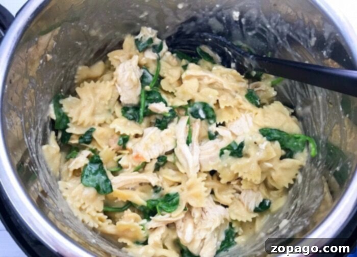 A bowl of pressure cooker chicken pasta, rich and creamy, with visible pieces of chicken, pasta, and vegetables, garnished with fresh herbs.