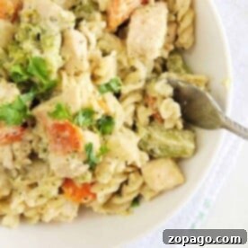A bowl of creamy Instant Pot chicken pasta with chunks of broccoli and carrots, garnished with cilantro. A fork is placed on the edge of the bowl.