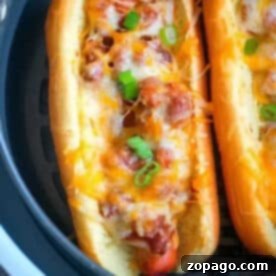 An air fryer hot dog topped with chili, melted cheese, and chopped green onions in a toasted bun.