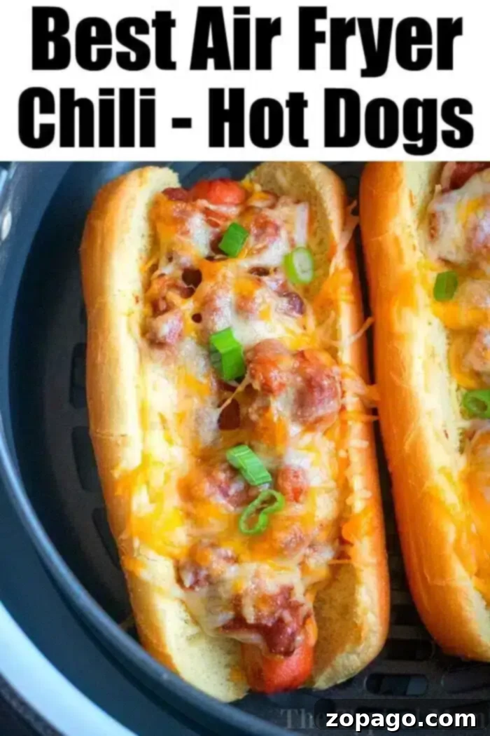 Perfectly Crispy Air Fryer Hot Dogs 9 Two hot dogs in buns are topped with chili, melted cheese, and chopped green onions. The air fryer hot dogs are situated in an air fryer basket. The text at the top of the image reads, "Best Air Fryer Chili - Hot Dogs.