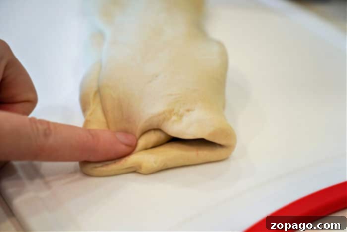 A hand expertly pressing the edge of a folded piece of dough on a white surface, preparing it to create an air fryer beef Wellington masterpiece.