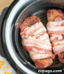 Perfect Air Fryer Steak 6 Two raw bacon-wrapped air fryer steaks sit in the basket, ready to be cooked to perfection.
