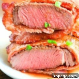 Close-up of a sliced, medium-rare air fryer steak garnished with chopped green onions on a white plate.
