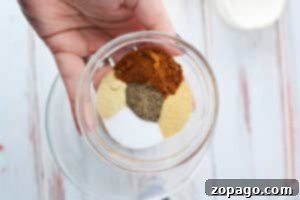 A hand holds a bowl of assorted spices and seasonings arranged in separate sections—perfect for learning how to cook steak tips in the oven with flavorful results.