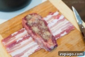 Perfect Air Fryer Steak 5 Air fryer steak, seasoned with spices, rests on bacon strips atop a wooden board with a knife nearby.