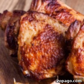 Roasted bone-in chicken thighs with golden-brown skin and garlic cloves sit invitingly on a wooden board, showcasing their crispy perfection achieved in the air fryer.