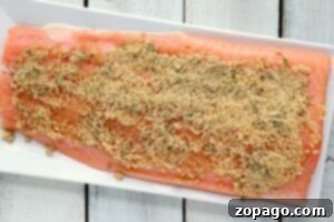 Raw salmon fillet, ready to transform into succulent perfection in the air fryer, is elegantly presented on a white rectangular plate, covered with a fragrant herb and breadcrumb mixture.
