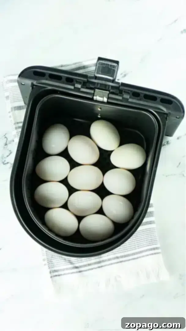 Discover how to make perfect air fryer hard boiled eggs with three distinct yolk consistencies. An ideal snack or protein-packed breakfast for any air fryer enthusiast. A black air fryer basket containing twelve white eggs, neatly arranged for making air fryer hard boiled eggs, is placed on a white and gray striped cloth on a marble surface, highlighting the ease and efficiency of air fryer cooking.