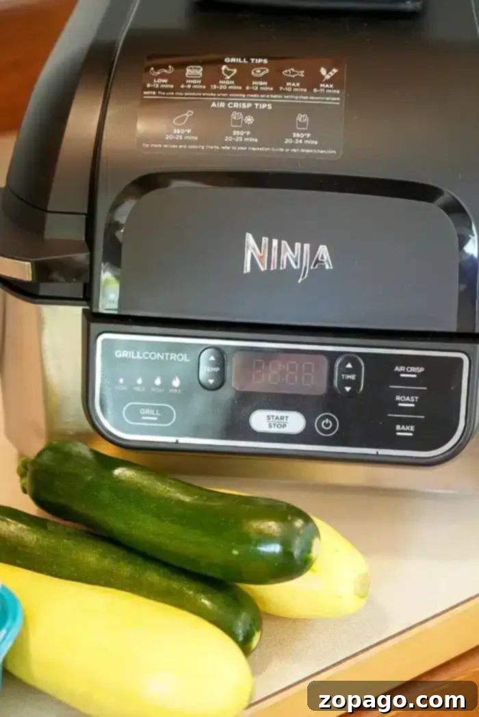 Preparing Ninja Foodi Grill Vegetables for Air Frying A Ninja air fryer is positioned on a kitchen counter, prepared to effortlessly cook air fryer vegetables. In front of the appliance, two fresh zucchinis and a yellow squash await preparation. The digital control panel on the air fryer displays various cooking options, and detailed grill and air crisp instructions are conveniently labeled on its lid.