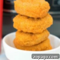 A stack of golden chicken nuggets, crisp and deliciously tender, sits in a small white bowl, perfectly cooked in the air fryer straight from their frozen state.
