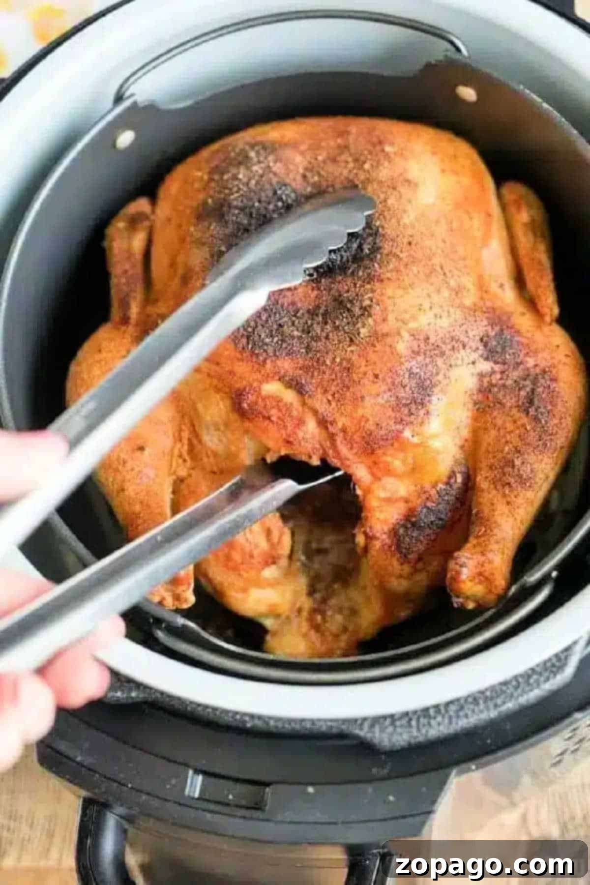A perfectly cooked, golden-brown air fryer whole chicken rests in its basket, ready to be served. Tongs gently lift a piece, highlighting the crispy skin and tender meat.