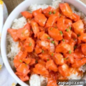 Bowl of white rice topped with pressure cooker apricot chicken, garnished with chopped green onions.