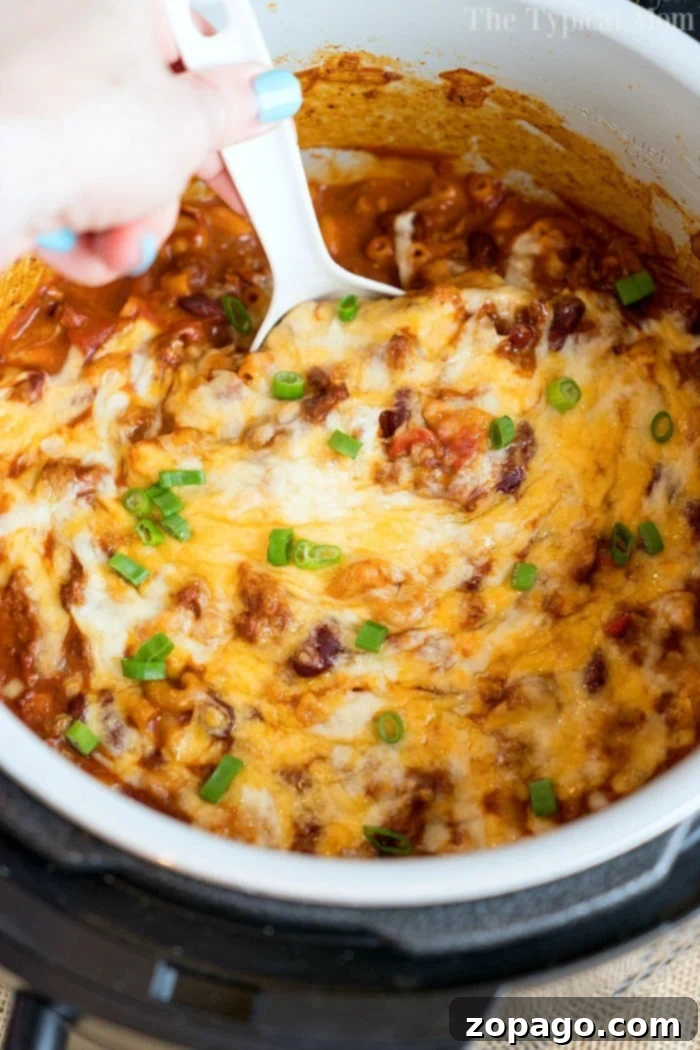 Ninja Foodi chili mac is so good! Packed with flavor and taking only 20 minutes to make in your Instant Pot or Ninja Foodi, you'll love it! #instantpotrecipes #instantpot #thetypicalmom #ninjafoodirecipes #ninjafoodi #chilimac #cheesy #casserole #pasta A top-down view of a vibrant pressure cooker cheesy chili mac, garnished with fresh green onions, showcasing its rich, comforting appeal.