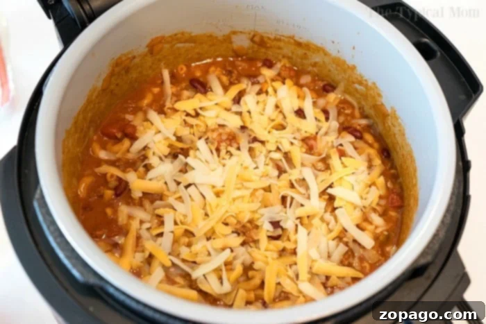 Pressure cooker cheesy chili mac is so good! Packed with flavor and taking only 20 minutes to make in your Instant Pot or Ninja Foodi, you'll love it! #instantpotrecipes #instantpot #thetypicalmom #ninjafoodirecipes #ninjafoodi #chilimac #cheesy #casserole #pasta A close-up shot of a cheesy chili mac dish, bubbling and golden brown, fresh out of the pressure cooker and topped with melted cheese.