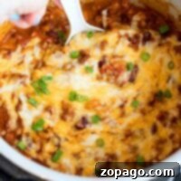 A hand stirs a pressure cooker cheesy chili mac dish, topped with melted cheese and vibrant green onions.