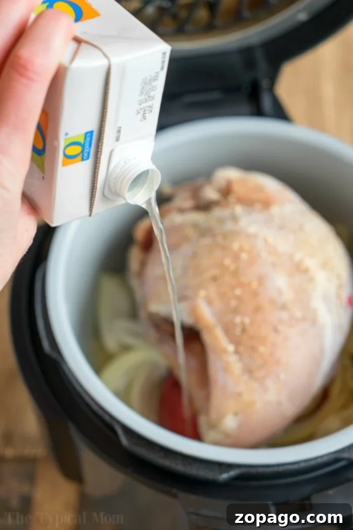 A whole pressure cooker turkey breast, seasoned and ready, in a Ninja Foodi with a measuring cup of broth.