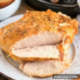 Sliced roasted turkey breast, prepared to perfection in a pressure cooker, rests on a white plate adorned with fresh herbs, with the Ninja Foodi subtly visible in the background.