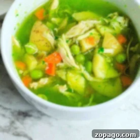 A comforting bowl of feel better soup, featuring peas, carrots, potatoes, and shredded chicken in a green broth, uses the convenience of an Instant Pot to bring warmth and nourishment to your table. Placed invitingly on a marble surface, it's perfect for those days when you need an extra hug.