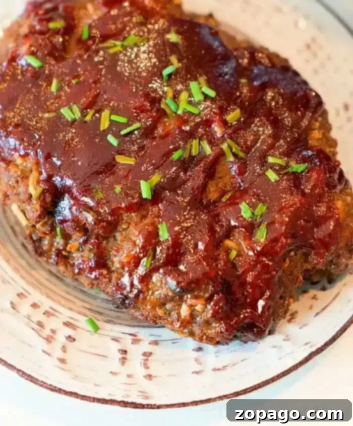 Perfect Ninja Foodi Meatloaf 2 A plated portion of Ninja Foodi meatloaf topped with a glossy layer of barbecue sauce and garnished with chopped chives. The meatloaf sits on a white ceramic plate with dark streak patterns.