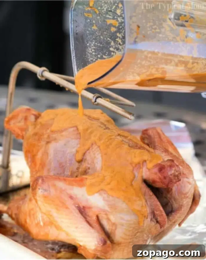 Herbed Turkey Butter Recipe 2 A raw turkey being generously coated with a rich, orange-hued wet rub from a blender, resting on a metal rack above a foil-lined pan, ready for enhanced flavor and cooking.
