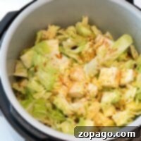 Chopped cabbage and noodles with spices simmering in a pressure cooker, positioned beside a spice container, showcasing the preparation.