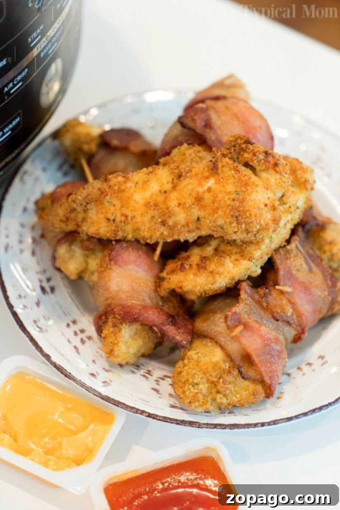 Air fryer chicken tenders wrapped in bacon are here for you to enjoy tonight! Easy 20 minute air fryer dinner idea even the kids will love. #airfryerrecipes #airfryer #ninjafoodi #chickentenders #chicken #homemade #chickenstrips #thetypicalmom #bacon Close-up of crispy air fryer chicken tenders wrapped in bacon