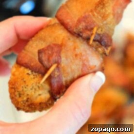 Close-up of a hand holding a crispy bacon-wrapped ninja foodi chicken tender secured with a toothpick.