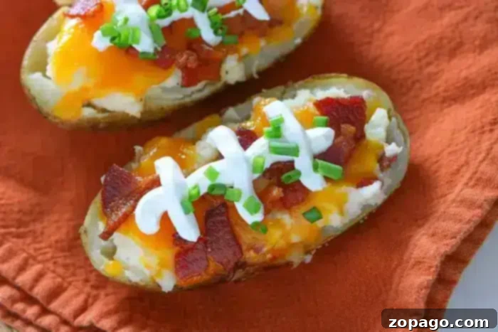 Make-Ahead Twice-Baked Potatoes 4 Two loaded baked potato halves, perfectly prepared for make-ahead twice-baked potatoes, rest on an orange cloth. Each is generously topped with a dollop of sour cream, crispy chopped bacon, melted cheddar cheese, and vibrant green onions, showcasing a delicious and impressive meal.