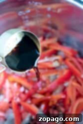 Soy sauce cascades from the measuring cup, enveloping the sliced red peppers in the pressure cooker to create a flavorful Chinese pepper steak.